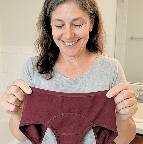 Woman holding a pair of maroon incontinence pants in a bathroom setting
