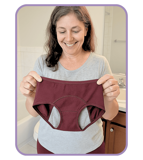Woman holding a pair of maroon incontinence pants in a bathroom setting